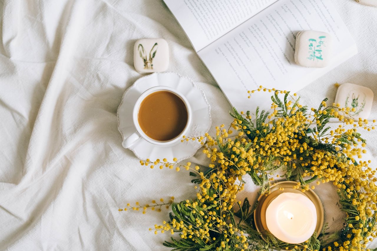 A serene flat lay featuring coffee, a book, and a candle with yellow flowers.